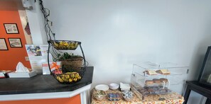 A counter with a fruit basket, a tray of pastries, and a display case with cookies. - Econo Lodge Lee - Great Barrington (Lee)