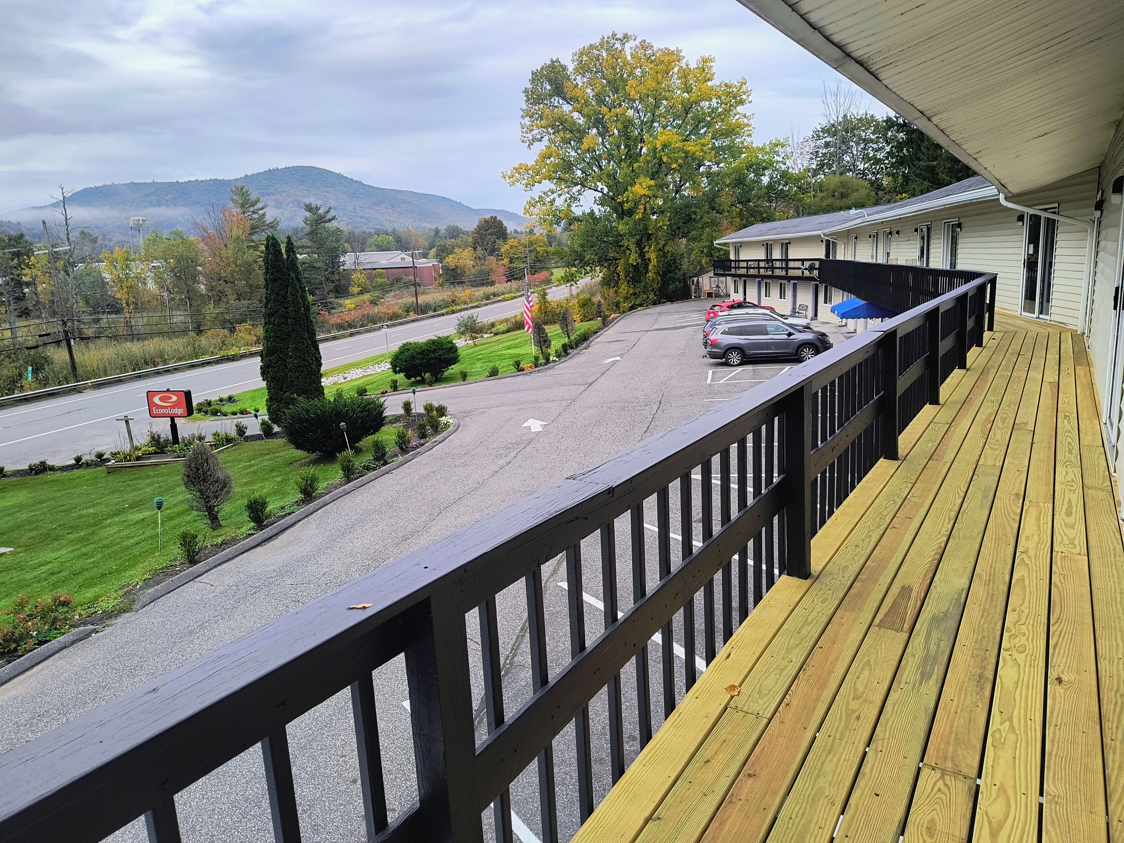 A wooden deck with a view of a road and a building with a white exterior.