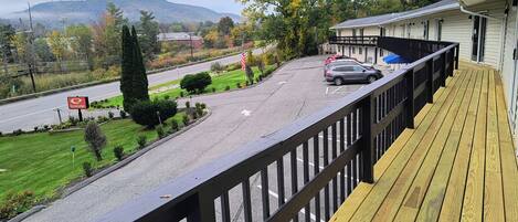A wooden deck with a view of a road and a building with a white exterior.