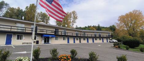 A motel with a flagpole, a blue awning, and a parking lot.