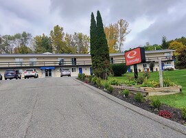 A motel with a parking lot, a signboard, and a lawn with plants.