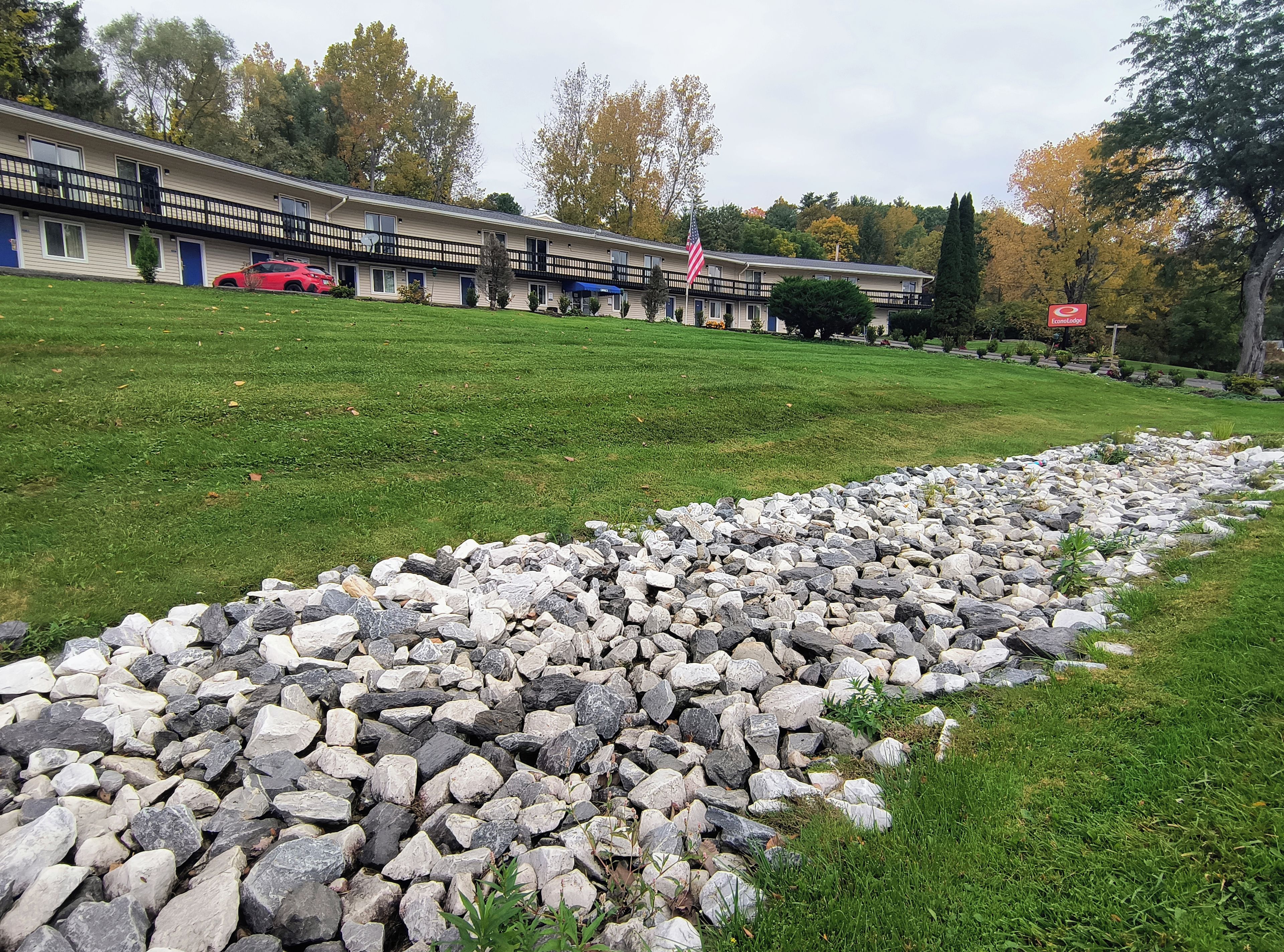 A motel with a lawn, a stone pathway, and a red car parked in front.