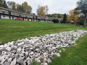 A motel with a lawn, a stone pathway, and a red car parked in front. - Econo Lodge Lee - Great Barrington (Lee)