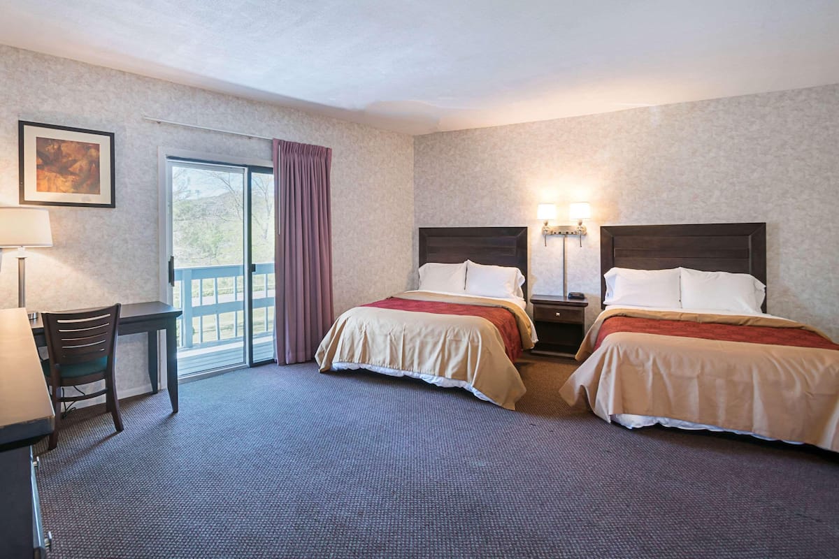 A hotel room with two beds, a desk, a chair, and a window with curtains.