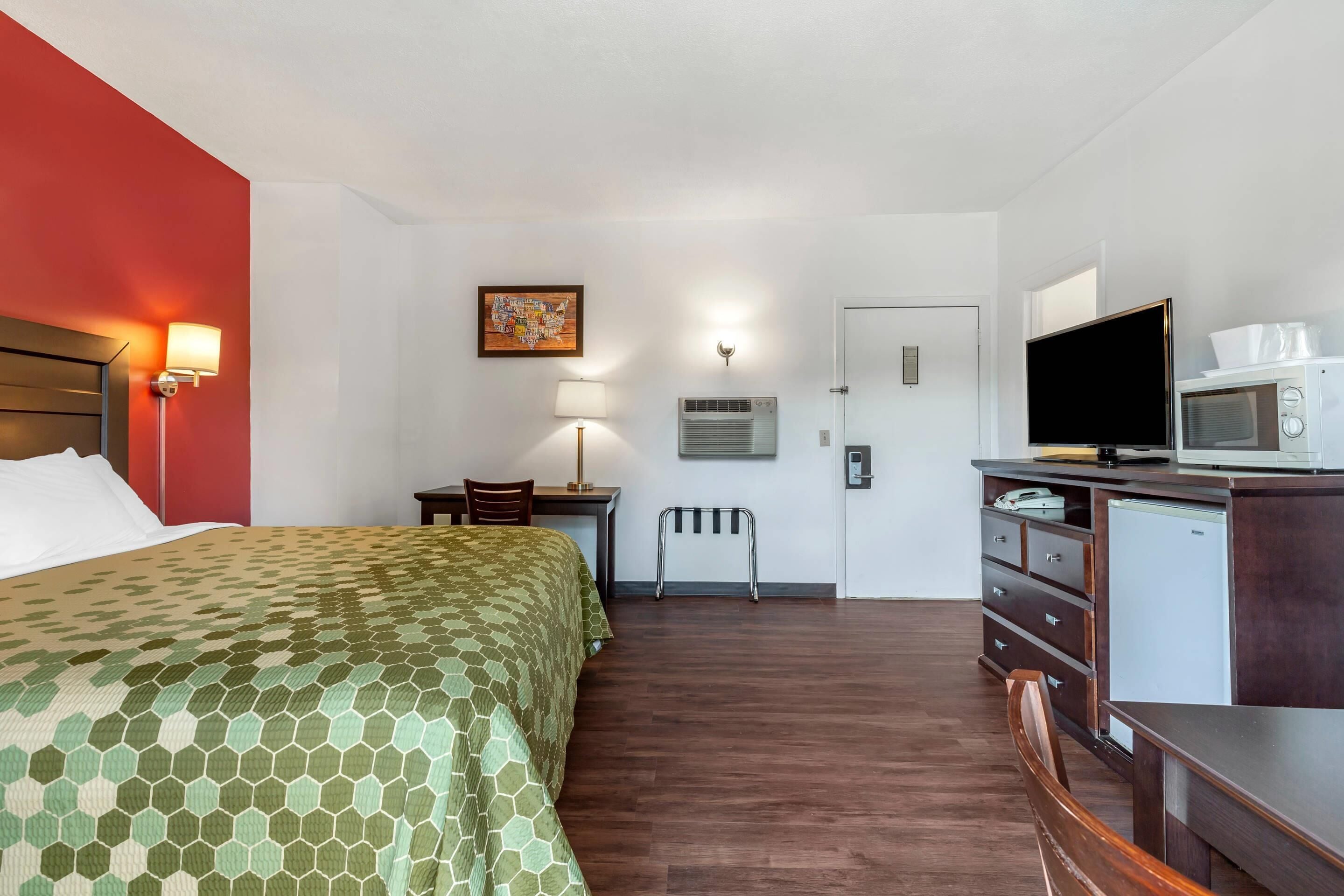 Ein Hotelzimmer mit Bett, Schreibtisch, Stuhl, Fernseher, Mikrowelle und kleinem Kühlschrank.