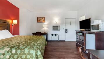 Ein Hotelzimmer mit Bett, Schreibtisch, Stuhl, Fernseher, Mikrowelle und kleinem Kühlschrank.