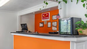 A hotel reception desk with an orange counter, a computer, a beverage cooler, and framed awards on the wall. - Econo Lodge Lee - Great Barrington (Lee)