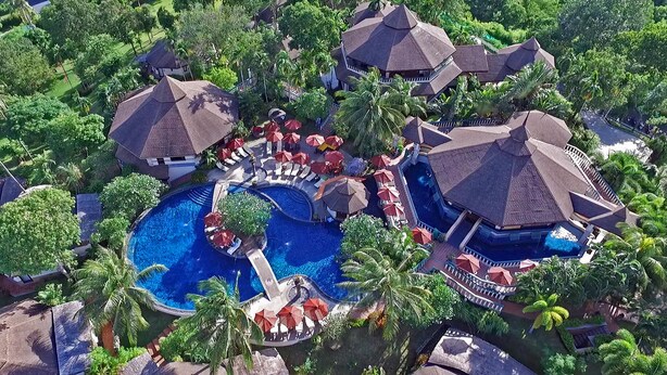 An aerial view of a resort with multiple buildings, a central swimming pool, and surrounding palm trees. - Mangosteen Ayurveda & Wellness Resort (Rawai)