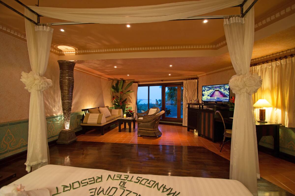 Een ruime kamer met een bed, een bank, een televisie en uitzicht op de omgeving.