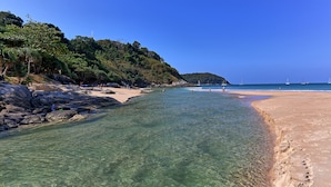 Ein Strand mit klarem Wasser, felsigem Ufer und einem bewaldeten Hügelhang.