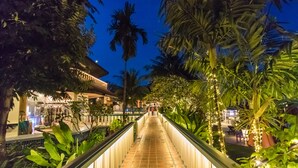 A nighttime walkway with a tiled path, surrounded by lush greenery and palm trees. - Mangosteen Ayurveda & Wellness Resort (Rawai)