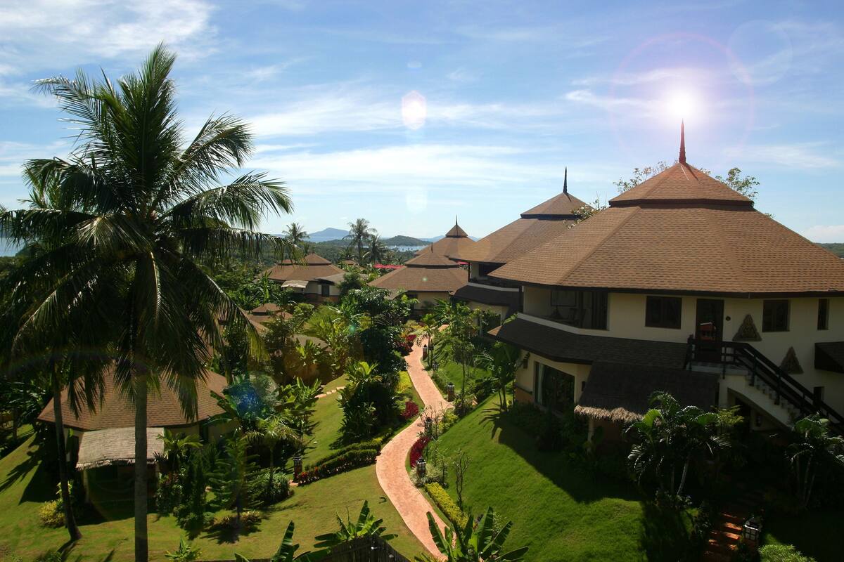 Een resort met meerdere bungalowgebouwen, een centrale pad en weelderige tropische beplanting.