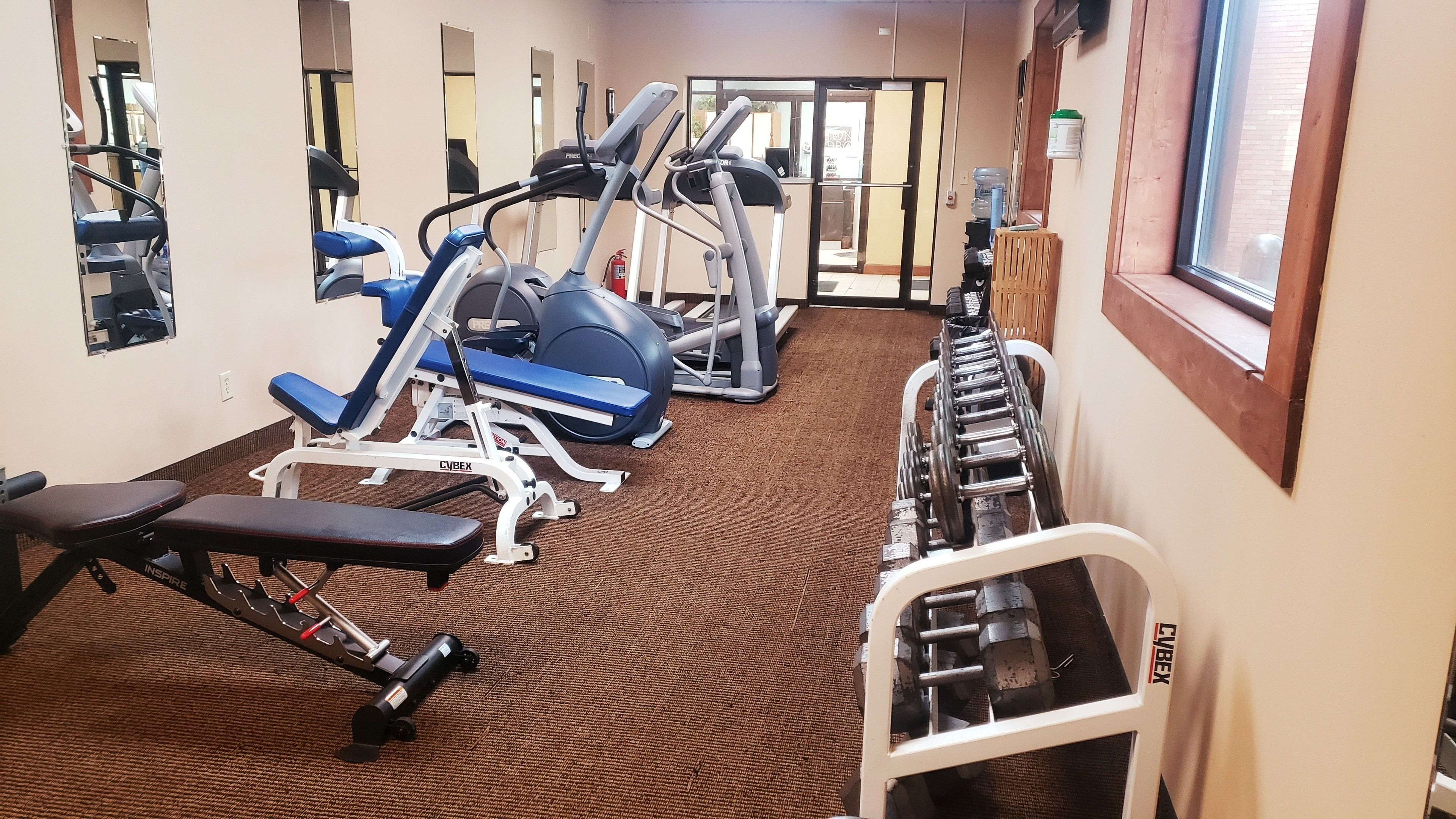 A gym with cardio machines, weight benches, and a water cooler.