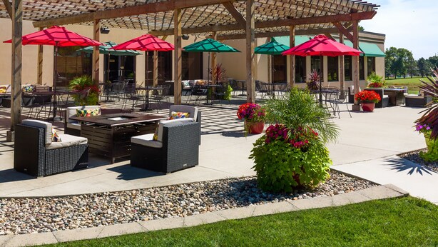 An outdoor patio area with wicker furniture, red and green umbrellas, and potted plants. - Lake Okoboji Resort & Conference Center (Okoboji)
