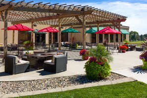An outdoor patio area with wicker furniture, red and green umbrellas, and potted plants.