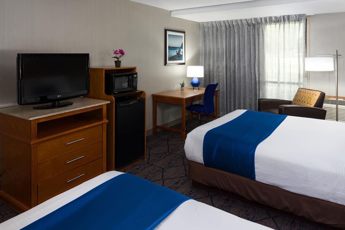 A hotel room with two beds, a desk with a chair, a television, a microwave, and a lamp.