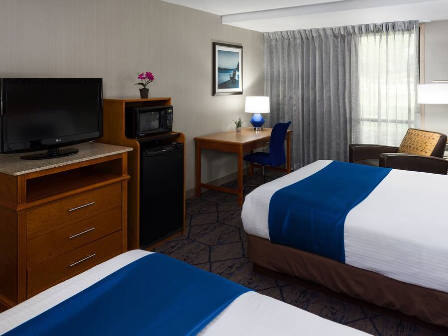 A hotel room with two beds, a desk with a chair, a television, a microwave, and a lamp.