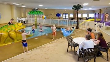 An indoor swimming pool area with water slides, a pool table, and seating for adults.