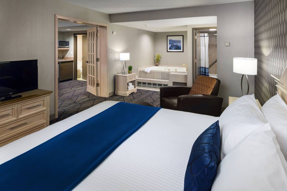 A hotel room with a large bed, a TV, a desk, a chair, a bathroom with a bathtub, and a shower.