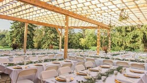 An outdoor covered patio with tables set for dining, surrounded by greenery. - Lake Okoboji Resort & Conference Center (Okoboji)
