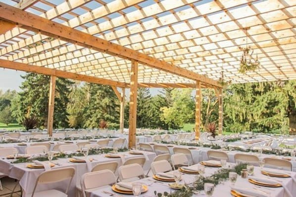 An outdoor covered patio with tables set for dining, surrounded by greenery.