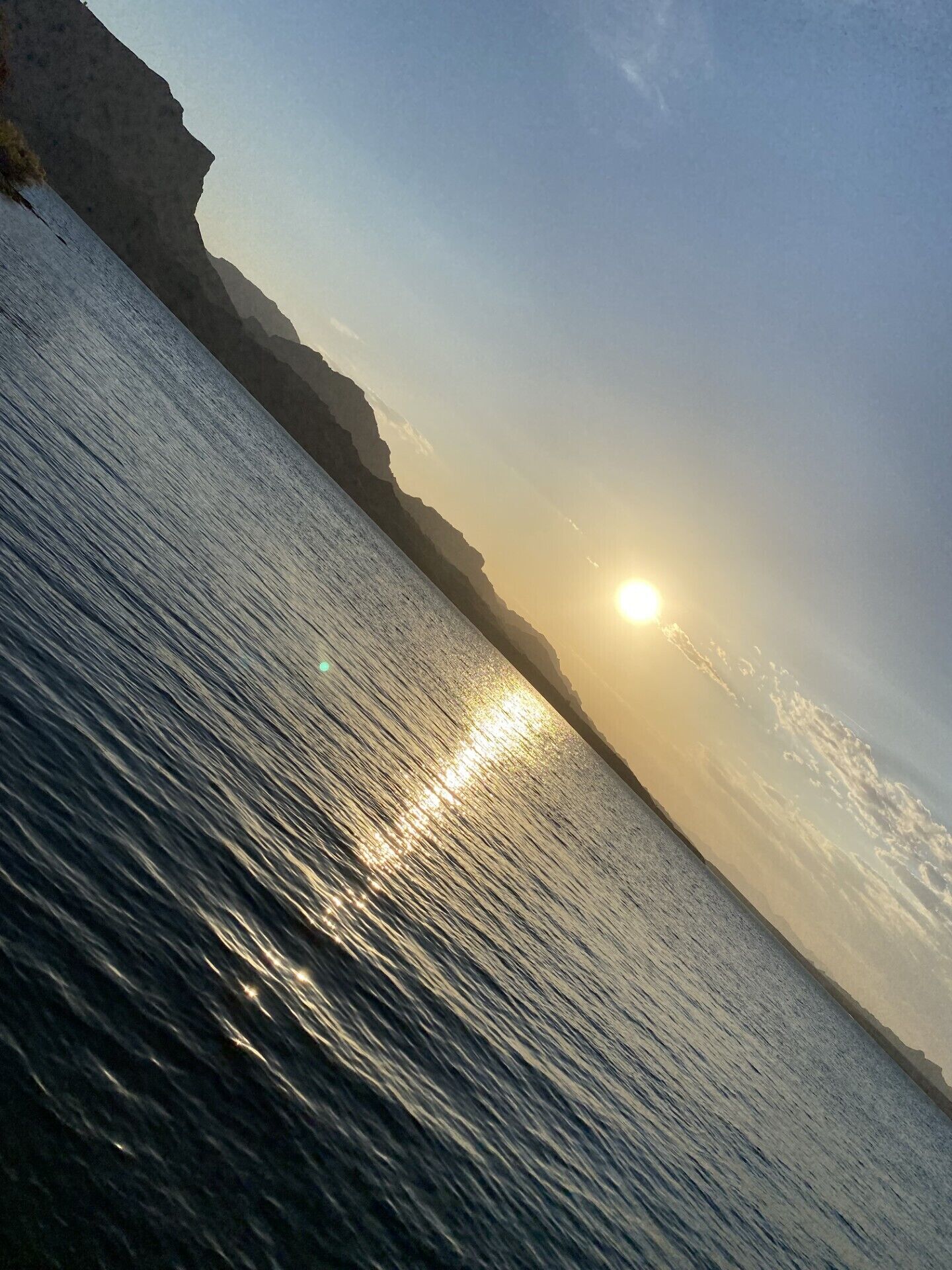 Paisaje costero con cielo despejado y el sol reflejándose en el agua.