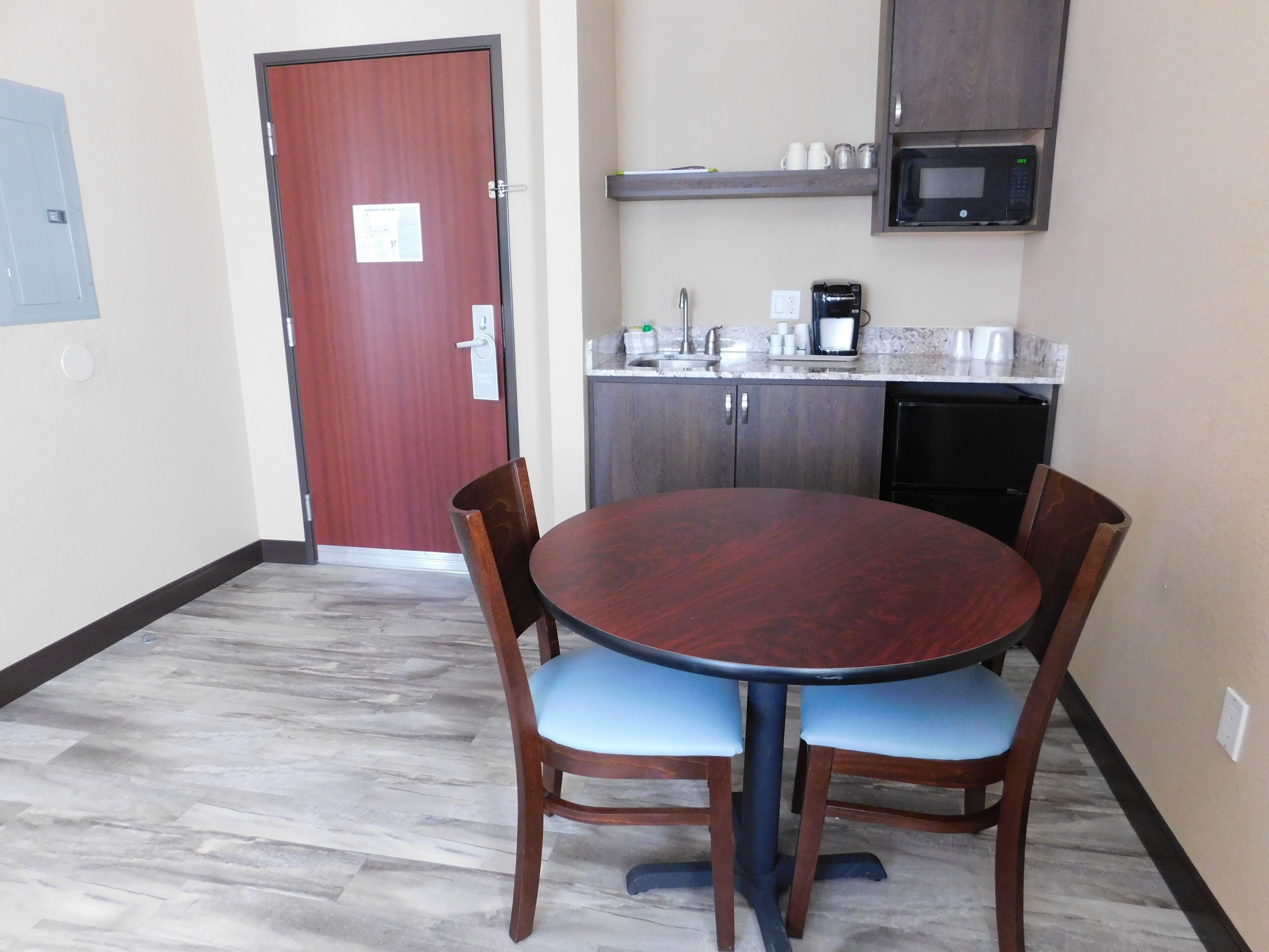 A small dining area with a round table and four chairs, a microwave above the counter, and a door with a sign.