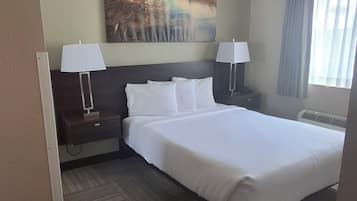 Un cuarto de hotel con una cama grande, dos mesitas de noche con lámparas, un cuadro en la pared y una ventana con cortinas.