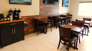 A restaurant with wooden tables and chairs, a coffee station, and artwork on the walls. - Island Suites (Lake Havasu City)