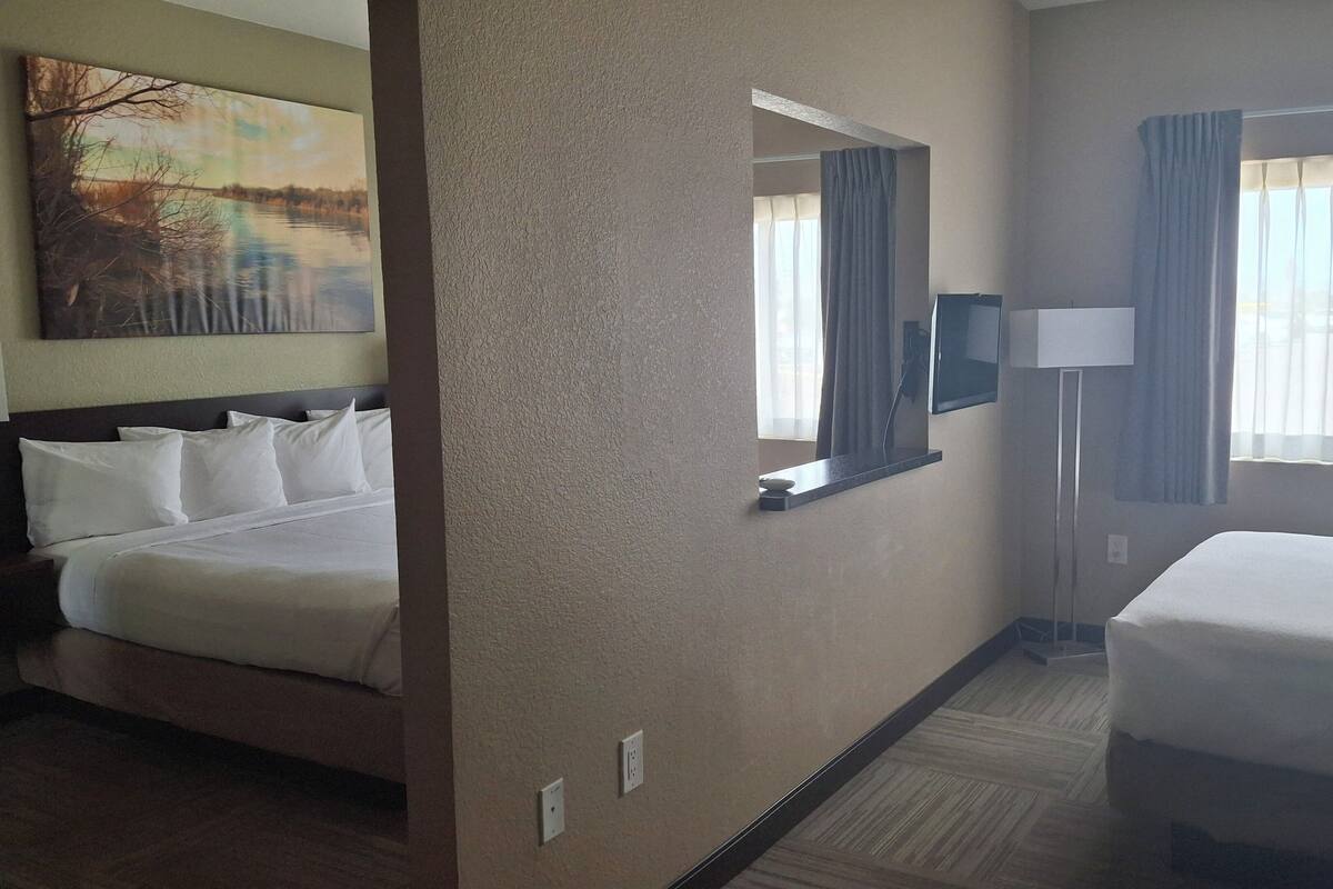 A hotel room with two beds, a large painting on the wall, a mirror, a lamp, and a view of the outdoors through the window.