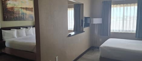 Une chambre d’hôtel avec deux lits, un grand tableau au mur, un miroir, une lampe et une vue sur l’extérieur par la fenêtre.