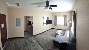 A hotel room with a ceiling fan, a sofa, a TV, and a window with curtains. - Island Suites (Lake Havasu City)