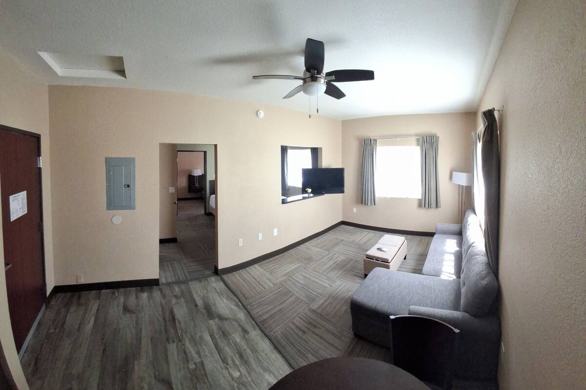 A hotel room with a ceiling fan, a sofa, a TV, and a window with curtains.