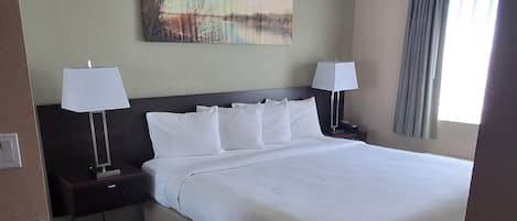 A hotel room with a large bed, two bedside tables with lamps, a painting on the wall, and a window with curtains.