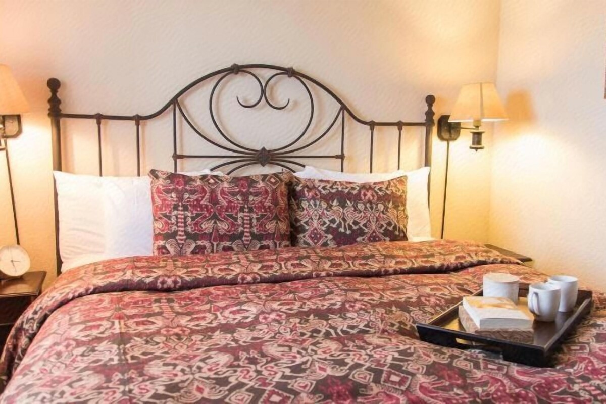 A neatly made bed with patterned bedding, a tray with cups and a book, and two bedside lamps on a nightstand.
