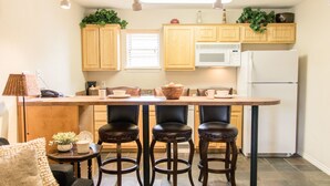 Una cocina con armarios de madera, un refrigerador blanco, un microondas y una zona con taburetes de bar.