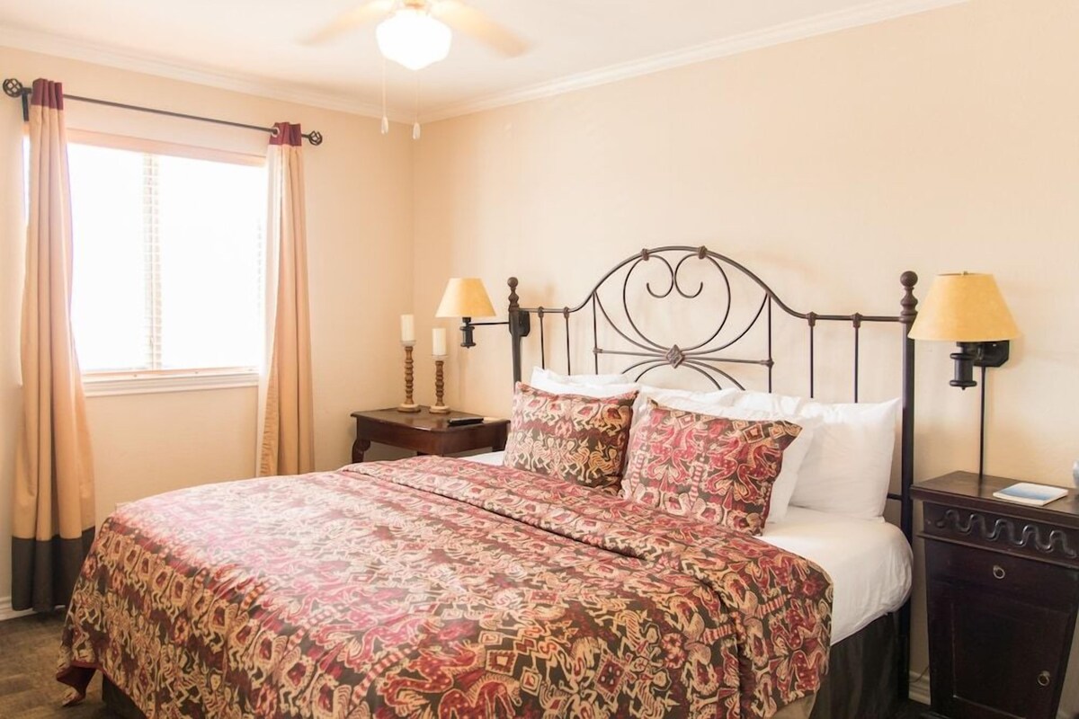 A bedroom with a bed, two bedside tables, a nightstand, a ceiling fan, and a window with curtains.
