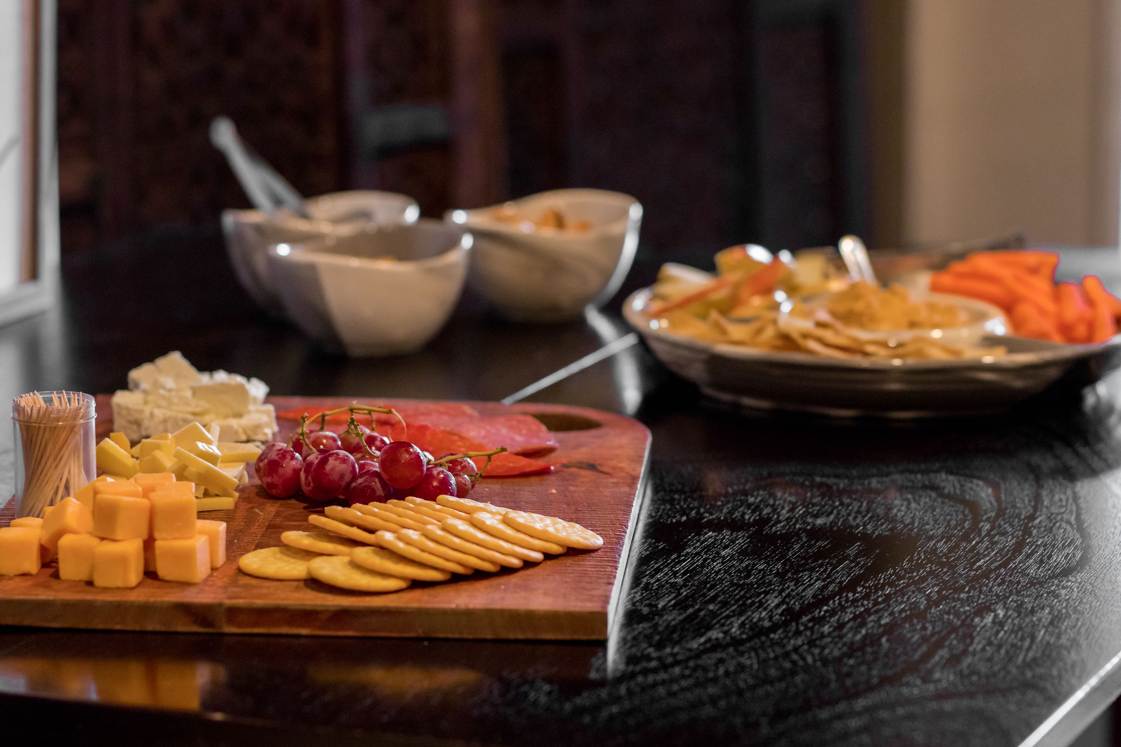 A wooden cutting board with cheese, crackers, and grapes.