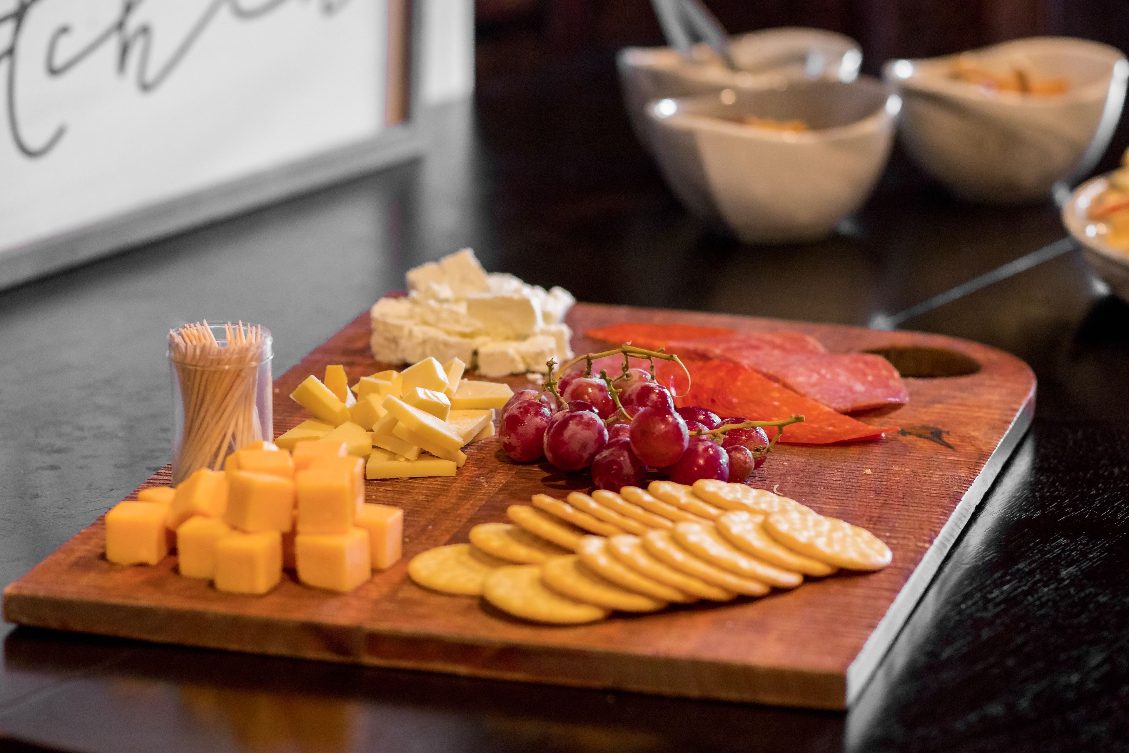 A wooden board with various cheeses, crackers, and grapes.