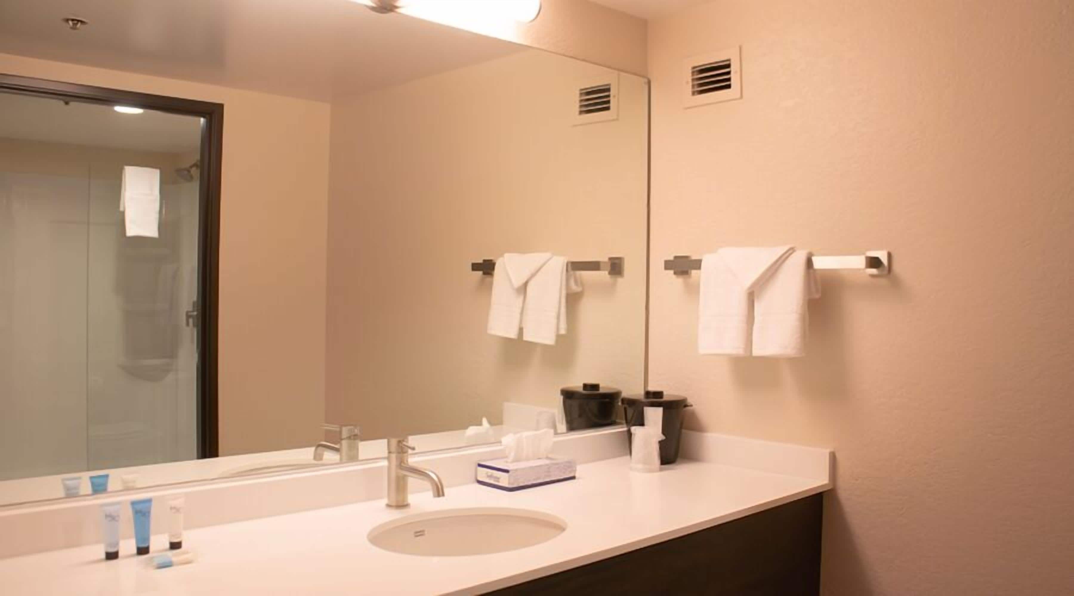 A hotel bathroom with a large mirror, a sink, and two towel racks.