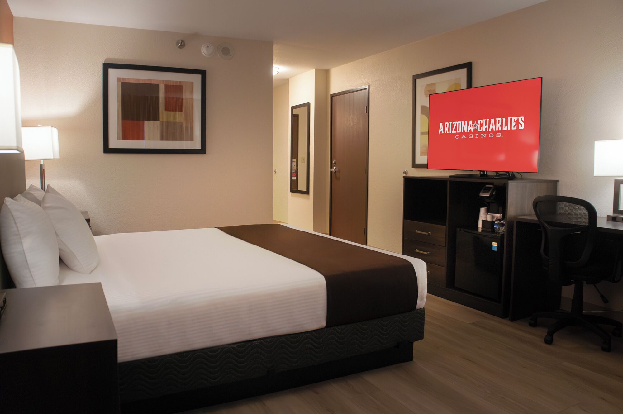 Een hotelkamer met een bed, een bureau, een stoel, een televisie en een ingelijste foto aan de muur.