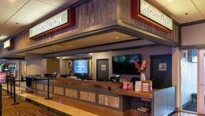 Un'area reception di un hotel con una scrivania per il check-in, uno schermo digitale che mostra informazioni e un cartello con gli orari di apertura.