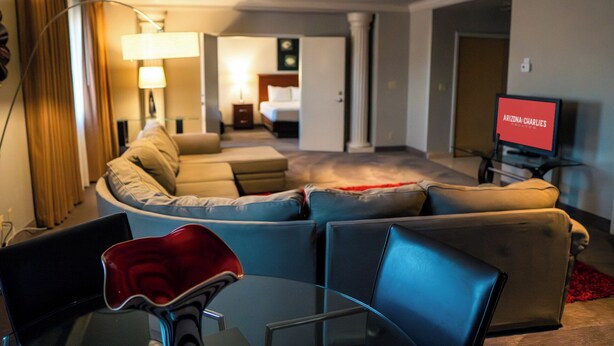 Una moderna camera d'albergo con un divano curvo, un tavolino in vetro e una televisione che mostra "ARIZONA-CHARLIE'S".