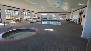 Ein großer, überdachter Pool mit Whirlpool, umgeben von Liegestühlen und Tischen, mit großen Fenstern für natürliches Licht.