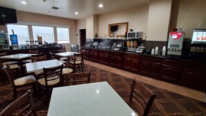 Ein Hotelrestaurant mit mehreren Tischen und Stühlen, einer Kaffeestation und einem an der Wand befestigten Fernseher.