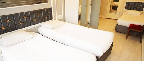 Une chambre d’hôtel avec deux lits simples, un miroir, une armoire et un petit coin salon.