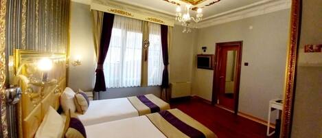 A hotel room with two beds, a chandelier, a television, and a mirror.