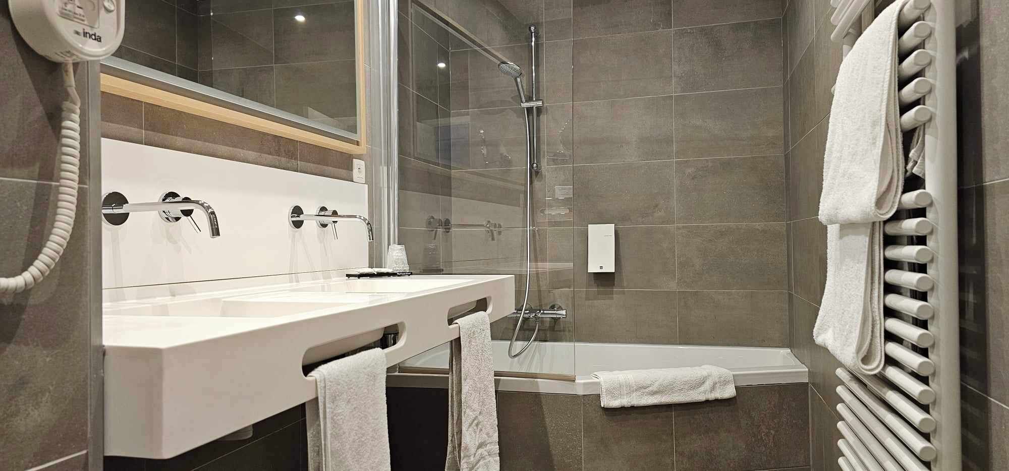 A modern bathroom with a glass-enclosed shower, a double sink vanity, and a built-in towel rack.