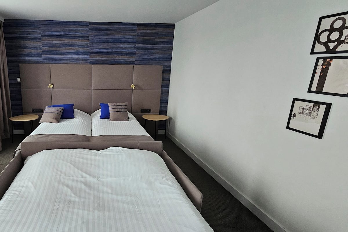 A hotel room with a large bed, two bedside tables, a blue chair, and a view of the city.
