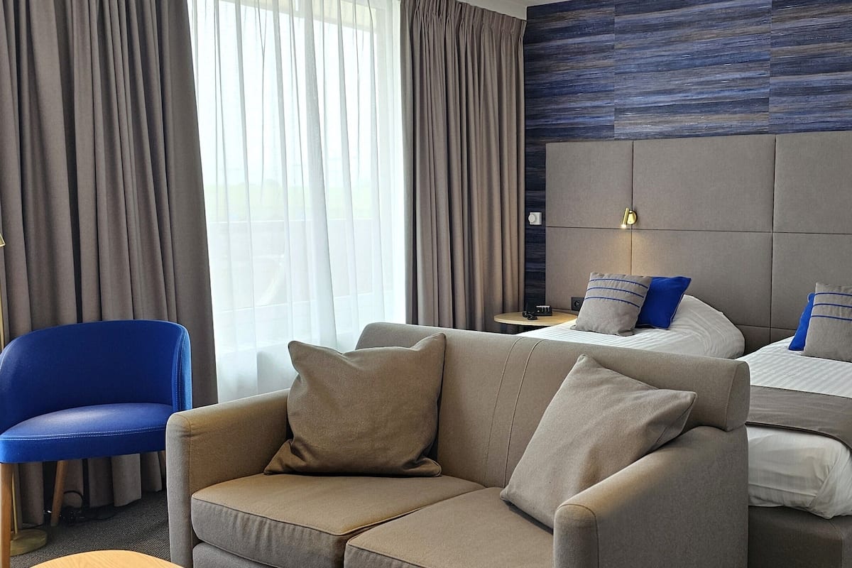 A hotel room with a large bed, two bedside tables, a sofa, and a chair.